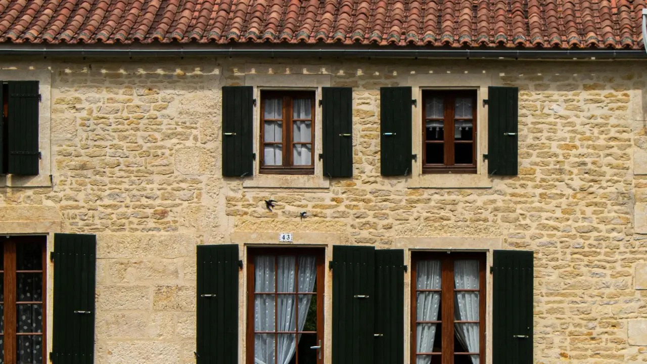 Gros plan sur la façade et la toiture d'une vieille maison en pierre. Le mur est impeccable, les pierres dorées et les joints refaits